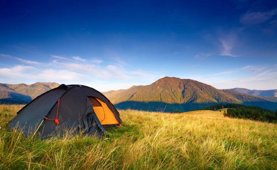 Camping tent on the mountain meadow after the dawn. Blue sky over hills